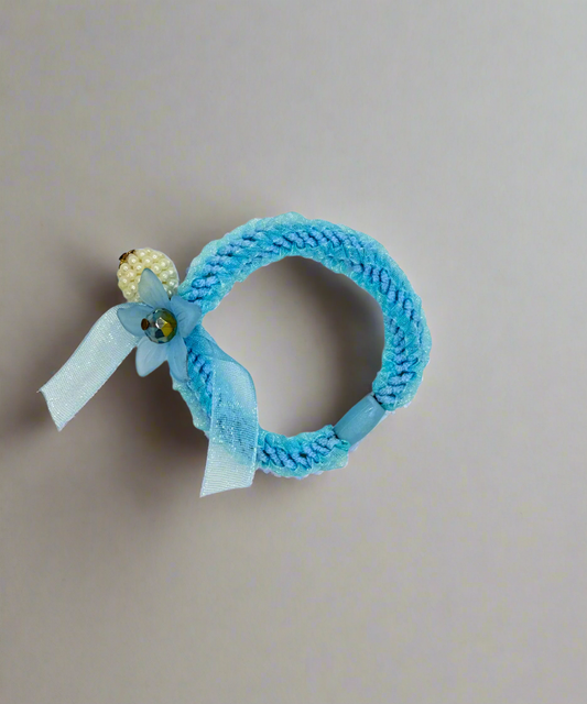 Light blue fabric scrunchie with a delicate bow, floral charm, and pearl bead accent, perfect for a stylish hair accessory.