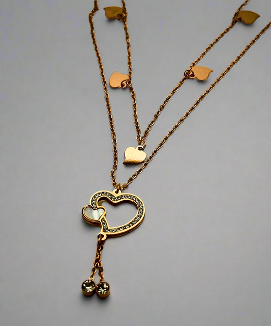 A gold-tone layered necklace featuring delicate heart charms, a crystal-embellished heart pendant, and dangling gemstone accents.