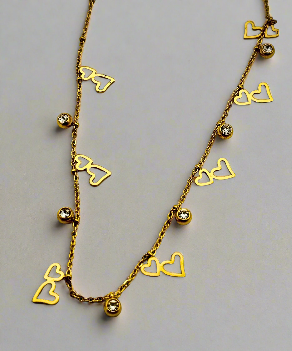 Gold chain necklace with delicate open-heart charms and sparkling crystal accents on a sleek white background.