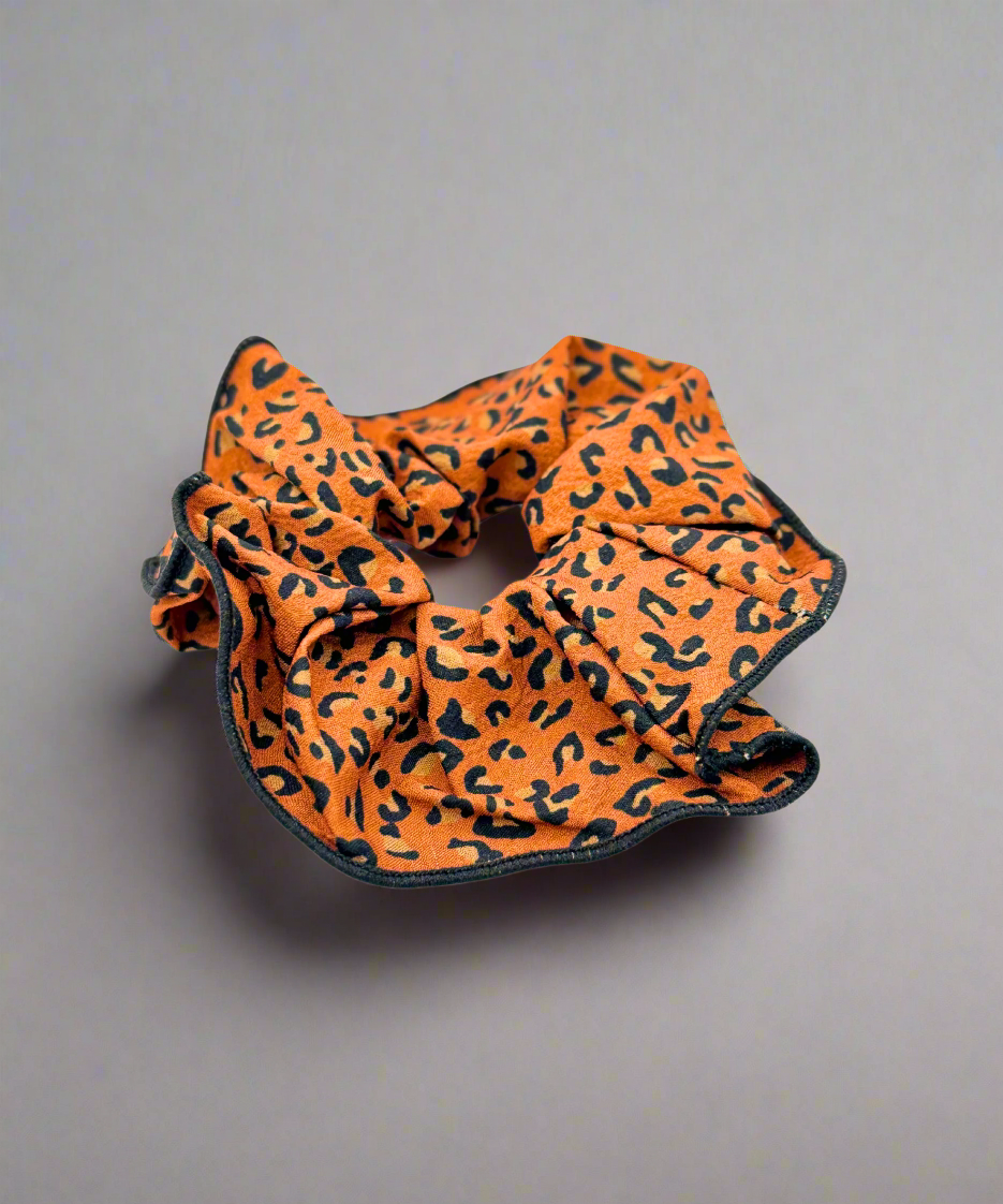 A stylish fabric scrunchie featuring a bold leopard print design, perfect for adding a trendy touch to any hairstyle. 