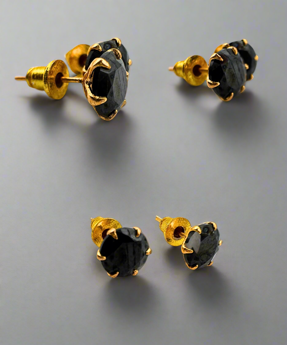 A pair of round-cut black stone stud earrings set in a gold-tone prong setting, offering a bold and sophisticated look.