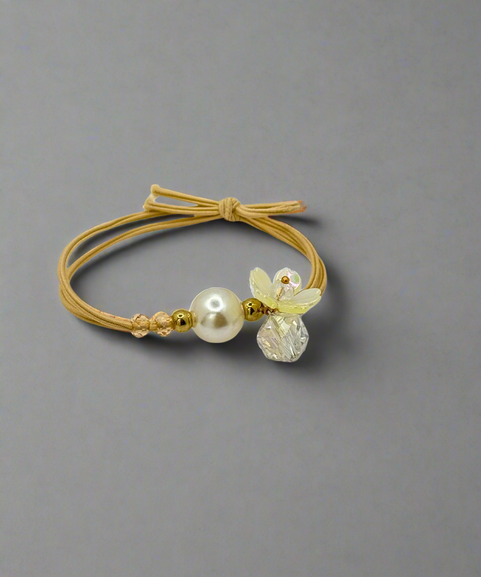 A stylish elastic hair tie featuring a delicate pearl, floral charm, and gold bead accents, perfect for an elegant look.
